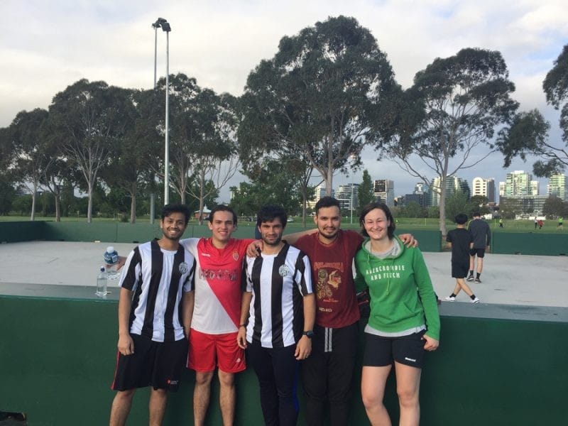 Dani y Melbourne cuatro amigos futbolistas que miran a la cámara sonrientes. Dos de ellos con el uniforme de fútbol y están en el campo de césped de fútbol
